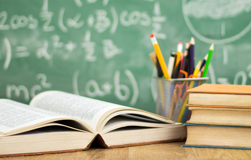 open book and pencils on desk in front of green chalkboard